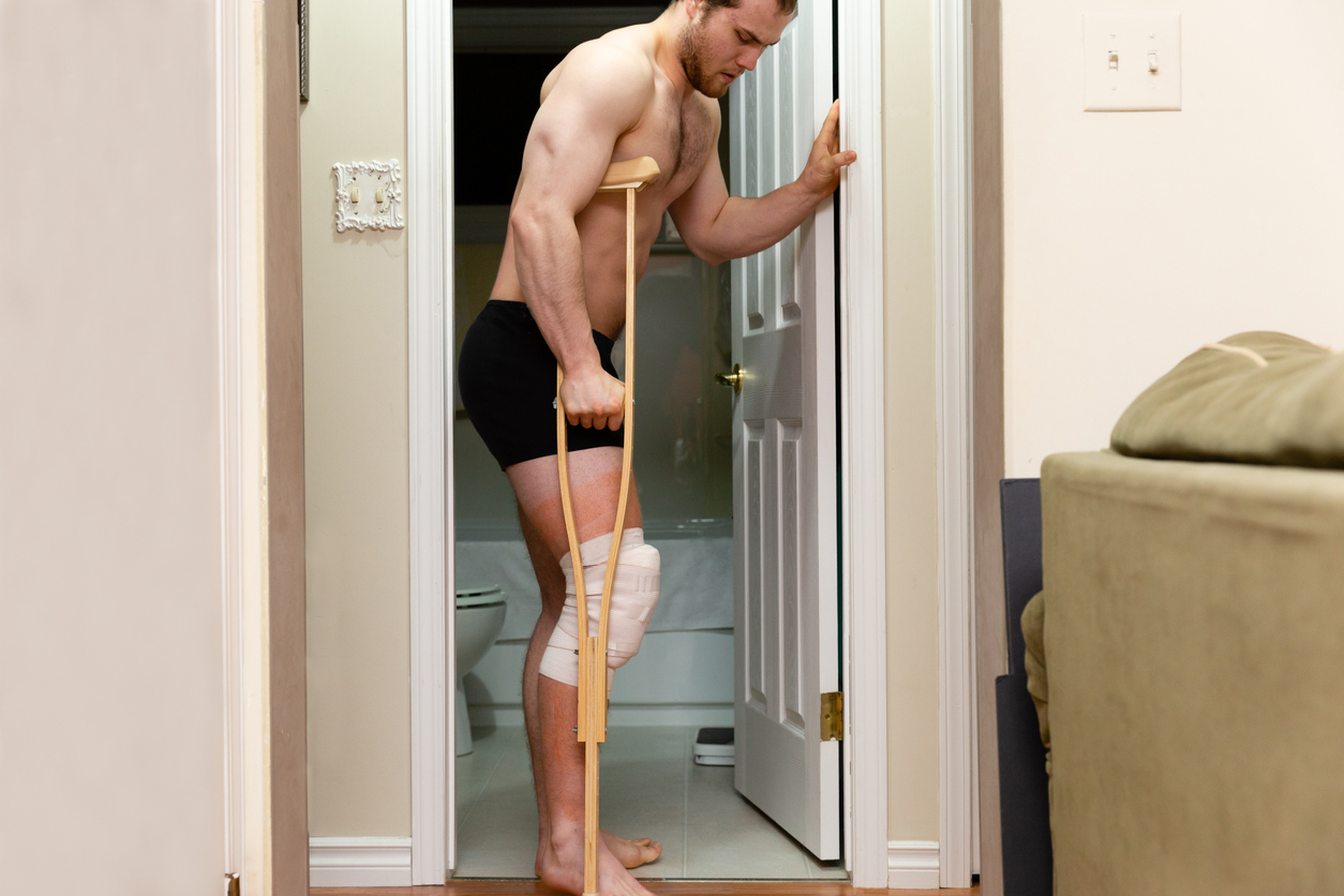 Man with knee bandage and crutch for ACL surgery recovery